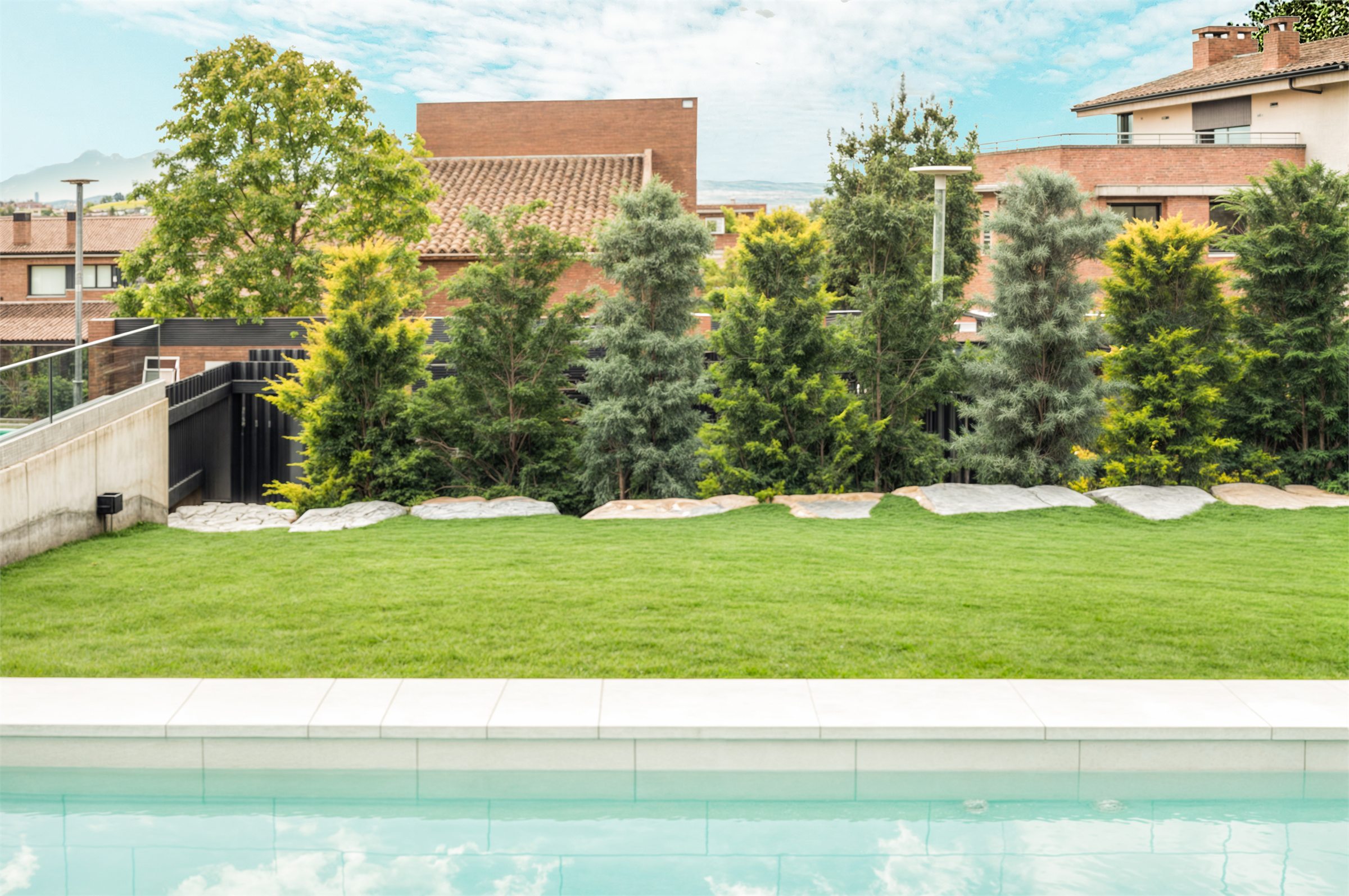 Jardí posterior amb la piscina en primer terme i el mur de formigó que conté el desnivell